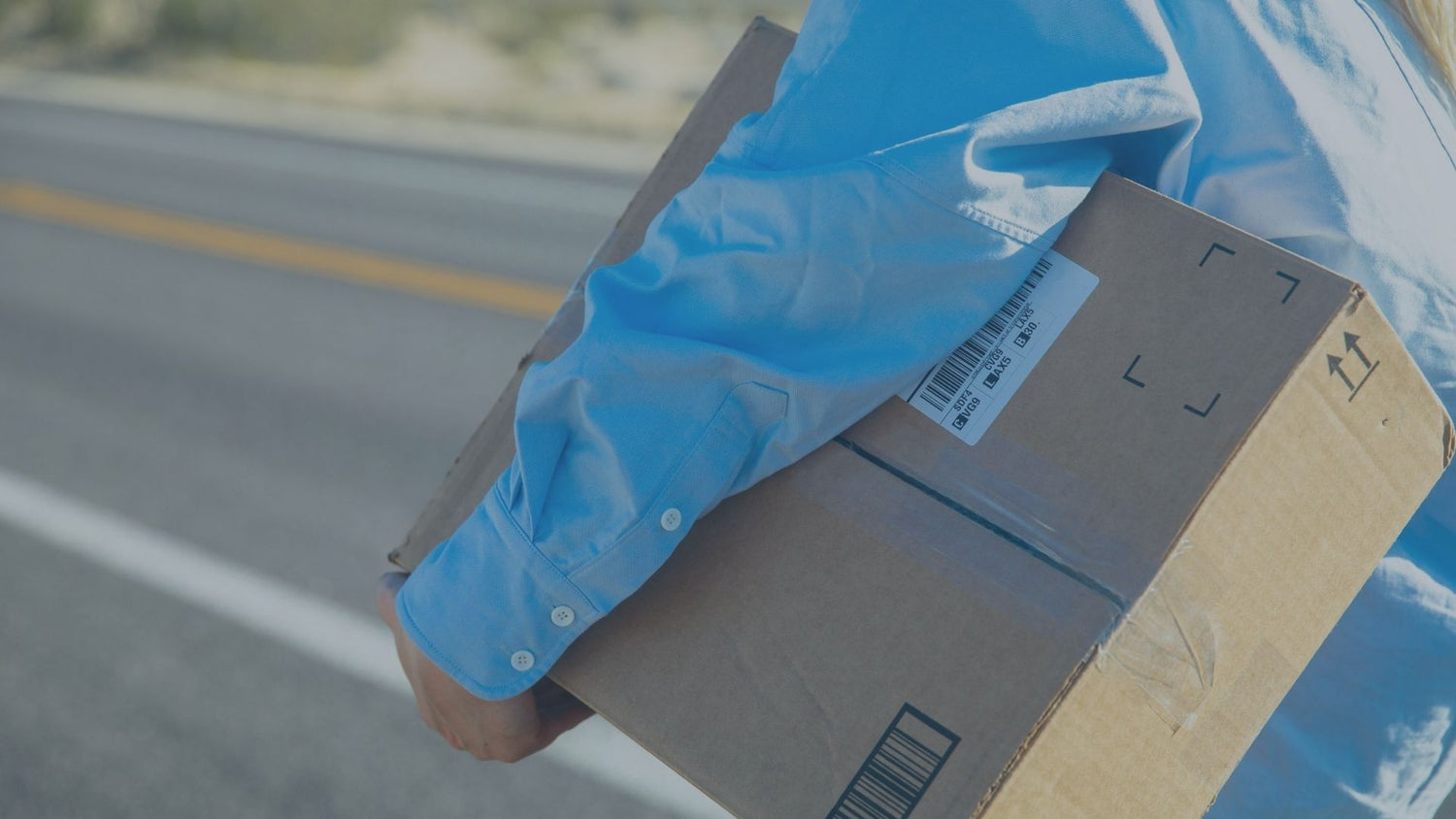 Eine Person in einem blauen Hemd trägt ein versandfertiges Paket mit sichtbarem Barcode-Label unter dem Arm, während sie an einer Straße entlangläuft, als Symbol für Paketversand und Logistikdienstleistungen.